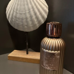 Parfym Paris Corner Qissa Delicious 100ml - Elegant parfymflaska i metallisk bronsfärg med räfflad design och en dekorativ etikett. Korken är matchande och har en lyxig känsla. Helt ny 🌸 Djuvlig doft nu till sommaren 🌸 Framsidan av flaskan har blivit något skadad, inget anmärkningsvärt, se bild🌸  Huvudnot: Mörk choklad, apelsin, vispgrädde. Hjärtnot: Kokosnöt, Marshmallow, Jasmin. 