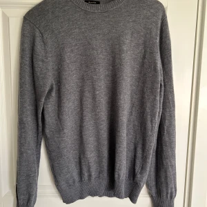 Massimo Dutti tröja - Säljer en stilren grå tröja från Massimo Dutti, tillverkad i en mjuk blandning av ull och kashmir. Tröjan har en klassisk rund hals och långa ärmar med ribbade muddar. Perfekt för kyligare dagar.