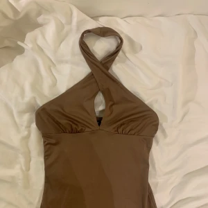 Brun klänning halterneck  - Snygg brun klänning med halterneck-design och en liten öppning framtill då den kryssas framför halsen. 
