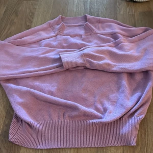 Ljusrosa stickad tröja från Amisu - Säljer en ljusrosa stickad tröja från Amisu. Tröjan har en ribbad krage och muddar vid ärmslut och nederkant. Perfekt för en mysig dag!