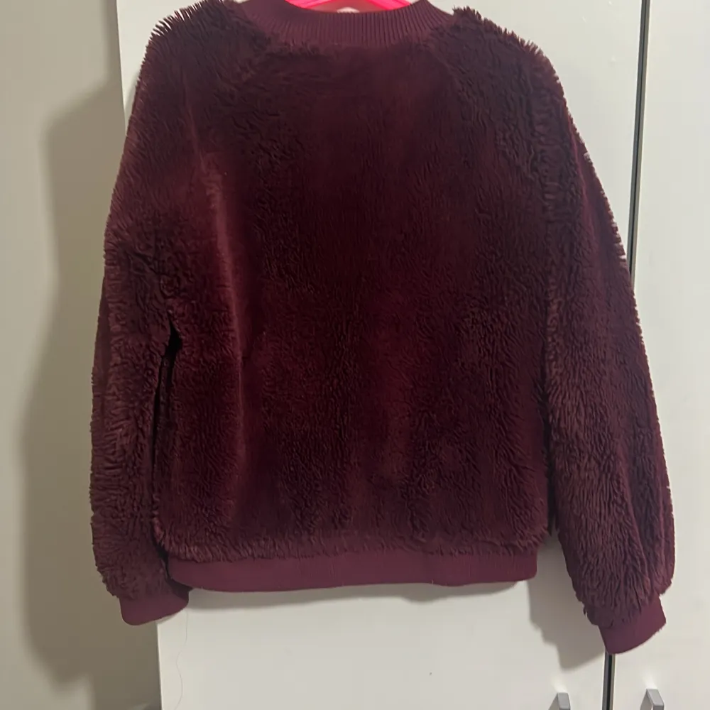 Mysig vinröd teddyjacka med dragkedja framtill. Jackan har långa ärmar och ribbade muddar vid ärmslut och nederkant. Perfekt för kyliga dagar.. Takit.