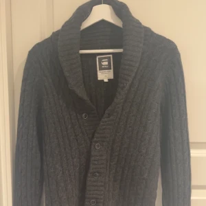 Stickad cardigan - Säljer en stilren grå stickad kofta från G-Star RAW. Koftan har en ribbad krage och knappar framtill. 
