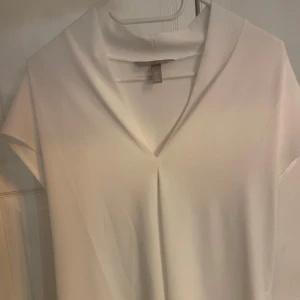 Vit blus med v-ringning - Säljer en stilren vit blus med v-ringning och korta ärmar. Perfekt för en elegant och avslappnad look.