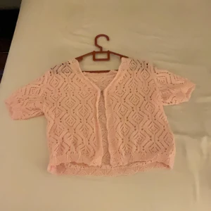 Rosa kofta - Söt rosa spetskofta med korta ärmar och ett fint mönster. Perfekt och skönt till sommaren. Koftan är öppen framtill och har en luftig design.