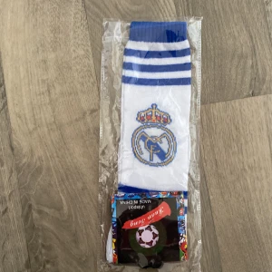 Vita och blå fotbollsstrumpor från Ruan Teng - Snygga vita fotbollsstrumpor med blå ränder och ett emblem på skaftet. Perfekta för fotbollsträningen eller att visa upp ditt stöd för laget. Tillverkade av Ruan Teng och kommer i en förpackning med sportigt tema.