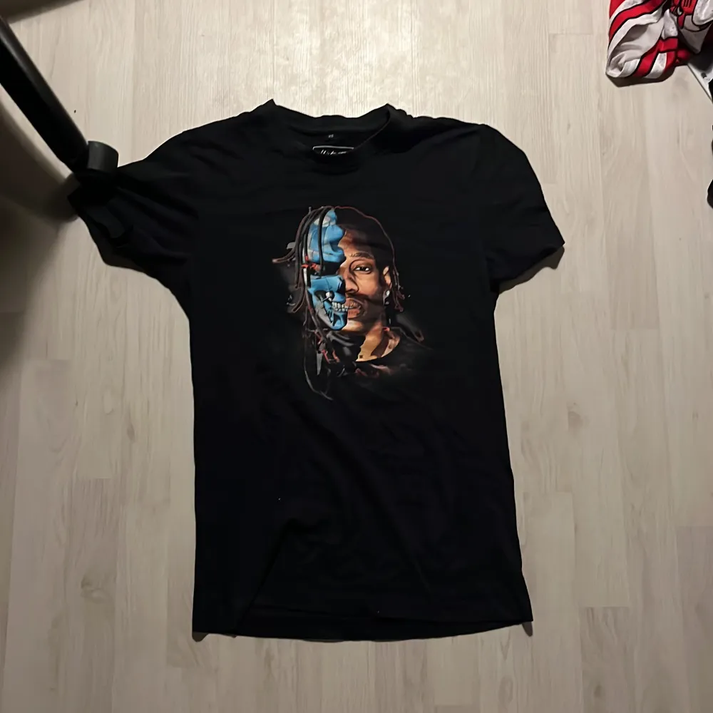 Snygg svart t-shirt med ett unikt tryck av ett ansikte i blått och rött. Perfekt för dig som vill sticka ut med en cool design. Kortärmad och i mjukt material.. T-paidat.