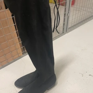Svarta mockastövlar - Snygga svarta stövlar i mocka med en stilren design. Perfekta för att ge en elegant touch till din outfit. De har en rund tå och är knähöga, vilket gör dem både praktiska och trendiga.