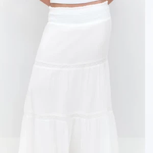 Vit långkjol - Säljer en vacker vit långkjol med volangdetaljer. Kjolen har en luftig och flödande design, perfekt för varma dagar. Den elastiska midjan ger en bekväm passform. Perfekt för en somrig look!💕