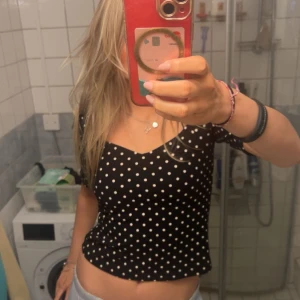 Svart prickig topp - Säljer en söt svart topp med vita prickar. Toppen har korta ärmar och en v-ringad design. Perfekt för en avslappnad stil.