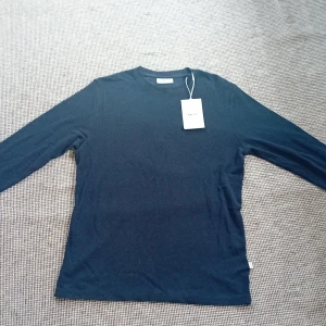 Mörkblå långärmad tröja från NN.07 - Säljer en stilren mörkblå långärmad tröja från NN.07. Perfekt för en avslappnad och snygg look. Tröjan har en klassisk rund hals och är tillverkad i ett mjukt material.