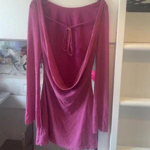 Rosa klänning med öppen rygg - Snygg rosa klänning med glittriga detaljer och en djup öppen rygg. Klänningen har långa ärmar och ett knytband i ryggen för extra stil. Perfekt för en festlig elr sommar kväll! Är i storlek S. 