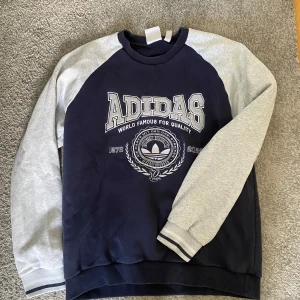 Vintage sweatshirt från Adidas - Säljer en snygg vintage sweatshirt från Adidas med tryck på framsidan. Tröjan har långa ärmar och ribbade muddar vid ärmslut och nederkant. Perfekt för en avslappnad stil.