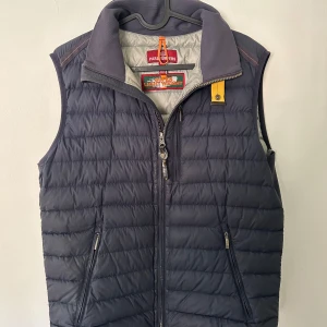 Mörkblå dunväst från Parajumpers - Snygg mörkblå dunväst från Parajumpers med dragkedja och hög krage. Perfekt för kyliga dagar och har praktiska fickor med dragkedja. Klassisk design som funkar till det mesta. Lite slitage på insidan av fickan och på själv dragkedjan men det inget man lägger märke till. Annat väldigt bra skick och perfekt nu till våren. Hör gärna av dig vid frågor😁