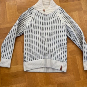 Vit och blå stickad tröja från KnowledgeCotton Apparel - Säljer en stilren vit och blå stickad tröja från KnowledgeCotton Apparel. Tröjan har ett snyggt mönster och en hög krage med en knappdetalj. Perfekt för kyliga dagar!