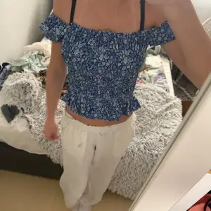 Säljer en söt blå offshoulder topp med blommigt mönster från Ydence. Toppen har en smockad design med volangdetaljer och tunna axelband. Perfekt för sommarens varma dagar!