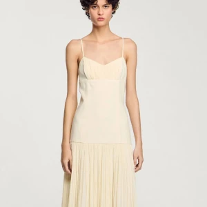 Champagnefärgad klänning från Sandro - champagnefärgad klänning från Sandro med smala axelband och plisserad kjol. Klänningen har en figurnära passform upptill. Nypris runt 4000kr