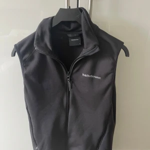 Svart väst från Peak Performance - Snygg svart väst från Peak Performance med dragkedja framtill. Perfekt för lager-på-lager och har en stilren design med diskret logga på bröstet.