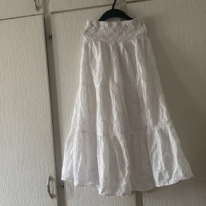 Vit långkjol från Gina Tricot - Säljer en vacker vit långkjol från Gina Tricot med broderade blommor. Kjolen har en elastisk midja för extra komfort och en luftig design som passar perfekt för varma dagar. Perfekt för en somrig look! 🌸
