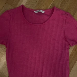 Rosa ribbad topp från Only - Säljer en snygg rosa ribbad topp från Only. Den har en rund halsringning och korta ärmar, perfekt för en avslappnad stil. Passar bra till både jeans och kjol.