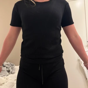 Svart ribbad topp - Säljer en stilren svart ribbad topp med korta ärmar. Perfekt för en enkel och snygg look. Passar bra till både jeans och kjol.
