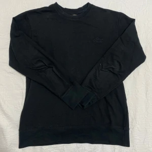 Svart tröja från Blend - Säljer en stilren svart tröja från Blend Denim. Tröjan har långa ärmar och en diskret broderad logga på bröstet. Perfekt för en avslappnad look. Storlek L men passar även M