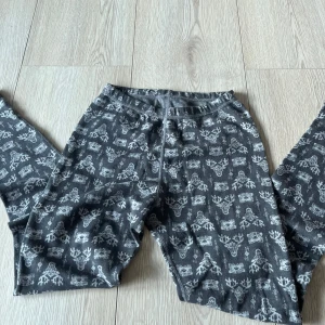 Grå underställ med mönster från Reima - Säljer ett par grå underställ från Reima med ett stilrent mönster av renar och snöflingor. Perfekta för kyliga dagar med sin mjuka och bekväma passform. Byxorna har en elastisk midja för extra komfort.