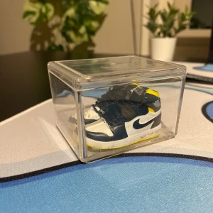 Mini nike skor - Säljer ett par miniatyr Nike Air Jordans i svart, vitt och gult. Skorna har snörning och texten 'NOT FOR RESALE' på sidan. Perfekt för samlare eller som dekoration.