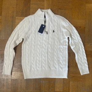 Vit stickad tröja från Ralph Lauren - Säljer en stilren vit stickad tröja från Ralph Lauren med kabelstickat mönster och dragkedja vid halsen. 