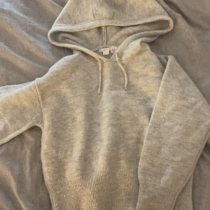 Ljusgrå stickad hoodie från Gina Tricot - Mysig grå hoodie från Gina Tricot i stickat material. Tröjan har huva med snörning och ribbad nederkant samt ärmslut.  Använd ungefär 2 gånger