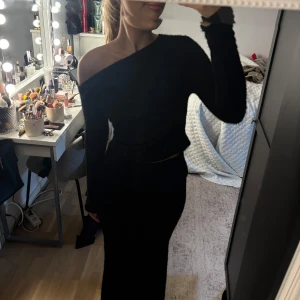 Svart oneshoulder croppad topp - Säljer en svart croppad topp med oneshoulder-design och långa ärmar. Toppen har en tight passform. Även en super fin mjuk lång kjol🤍 det är ett sett:) hela settet för 130kr. 
