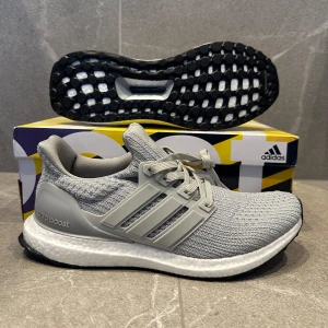 Grå Adidas Ultraboost  - Snygga grå Adidas Ultraboost sneakers med stickad ovandel och klassiska tre ränder på sidan. Skorna har vit Boost-sula för extra komfort och svart yttersula. Perfekta för dig som vill ha både stil och funktion i vardagen.