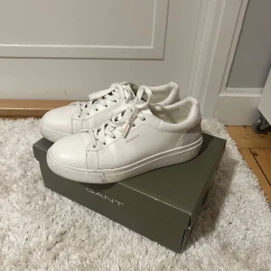 Vita sneakers från GANT i skinn - Snygga vita sneakers från GANT i skinn med detaljer i mocka baktill. Klassisk låg modell med rund tå, platt sula och snörning. Perfekta för en clean och stilren look. Märkeslogga på sidan och bak på hälen. Endast använda 1-2 gånger därav priset. Fråga vid fler bilder eller andra funderingar!😊