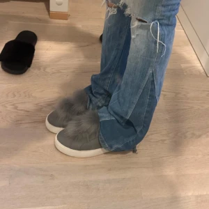 Grå sneakers med pälsdetalj - Grå sneakers från Steve Madden med vit platt sula och fluffig pälsdetalj på ovansidan. Skorna har rund tå och är tillverkade i mocka med inslag av syntet. Perfekt för dig som vill sticka ut med en unik och trendig look. Älskar skorna men dem är tyvärr för stora byter gärna mot en mindre storlek