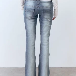 Slutsålda gina bootcut jeans - Snygga bootcut jeans i ljusblå tvätt med slitningar och klassiska femficksdetaljer. Jeansen har låg midja och är tillverkade i mjuk denim med lite stretch för skön passform. Perfekta för dig som gillar en retro vibe och vill ha ett par jeans som sticker ut.