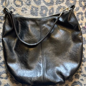 Ny snygg väska från Stradivarius  - Snygg ny svart axelväska från Stradivarius Väskan har en axelrem med snygga stora silverfärgade metallringar och den stängs/öppnas med en silverfärgad dragkedja Det är en mjuk modell med innerfoder Den har ett stort rymligt fack + ett mindre fack med dragkedja Den är helt ny och oanvänd  Mått: H38-40/B45. Köpt på Stradivarius i Lissabon