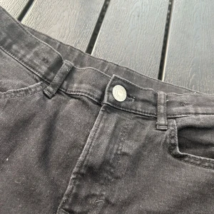 Svarta jeans med raka ben slim fit - Säljer ett par svarta jeans med klassisk femficksdesign och raka ben. Jeansen har bälteshällor, knappstängning och är tillverkade i ett mjukt bomullstyg med lite stretch. Perfekta till sneakers eller boots och funkar året runt.
