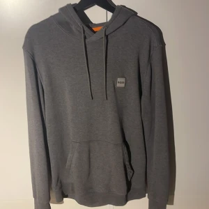 Grå hoodie från BOSS  - Snygg grå hoodie från BOSS med klassisk huva och snörning. Anledningen till att jag säljer är för att Den är för stor på mig.