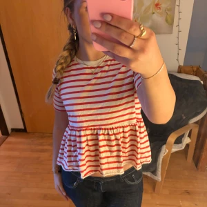 Randig blus med volang från Zara - Säljer en söt blus från Zara i storlek M med röda och vita ränder. Toppen har rund hals, korta ärmar och en volang nedtill. Aldrig använd🩷