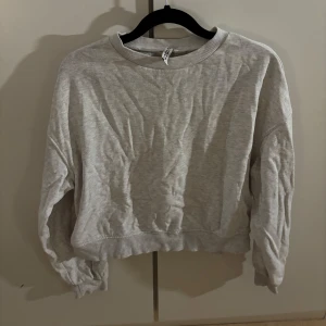 Ljusgrå sweatshirt från H&M Divided - En basic ljusgrå sweatshirt från H&M Divided i storlek S. Tröjan har rund halsringning, långa ärmar och ribbade muddar vid hals, ärmslut och nederkant. 