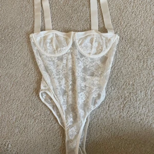 Vit spetskorsett från Muséra - Säljer en superfin vit korsett från Muséra med breda axelband och transparent spets med blommigt mönster. Toppen har bygelkupor för extra stöd och en riktigt snygg, feminin look. Perfekt att styla med jeans eller kjol för en trendig outfit.
