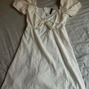  klänning - Supersöt vit klänning med broderade detaljer. Klänningen har knyt framtill och ett fint hålmönster över hela tyget. Perfekt för sommarens alla tillfällen💗