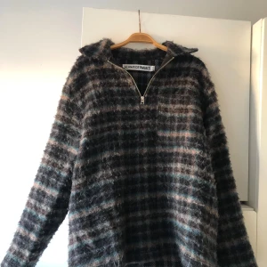 Rutig halvzip tröja från Schnayderman's - Mysig rutig tröja från Schnayderman's med halv dragkedja och hög krage. Färgerna går i mörkblått, grått och inslag av brunt. Tröjan är långärmad och har en fluffig, stickad känsla som passar perfekt till kyliga dagar. 