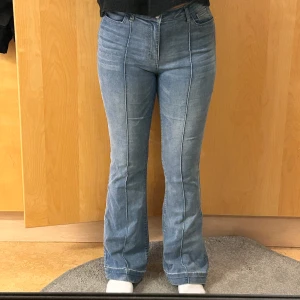 Blå bootcut jeans med pressveck - Snygga blå Mid-waist jeans med bootcut-modell och markerade pressveck längs benen. Jeansen har klassisk femficksdesign, bälteshällor och stängs med dragkedja och knapp. Perfekta för dig som gillar en retrovibe och vill ha ett par jeans som sticker ut. 