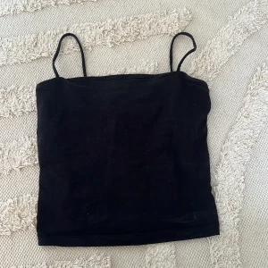 Svart croppad linnetopp Gina Tricot - En svart, croppad linnetopp från Gina Tricot med tunna axelband. Toppen är tight och har en enkel, stilren design.