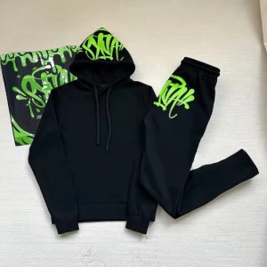 Svart och grön Syna World Tracksuit - Svarta mjukisbyxor med fett neon-grönt graffiti-tryck på ena benet. Sköna resårer vid midja och benslut, perfekt för chill eller streetwear. Materialet känns mjukt och flexibelt, och trycket ger en riktigt cool vibe.