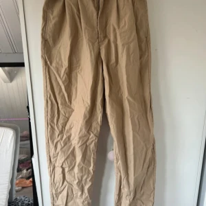 Beige tapered byxor från Levi's - Säljer ett par beige byxor från Levi's Premium i modellen High Loose Taper. Byxorna har hög midja och en loose passform som smalnar av nedtill. Tillverkade i mjuk bomull, perfekta för en chill och avslappnad stil. Klassisk knappstängning och fickor både fram och bak.