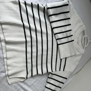 Vit och svart randig stickad tröja 157 - Vit stickad tröja från 157 i storlek XS med svarta ränder. Tröjan har lång ärm, ribbade muddar och bred ribbad nederkant med slits i sidorna. Klassisk rund halsringning och mjukt material som känns skönt mot huden.