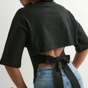 Svart topp från nelly - Snygg svart bolerotopp med öppen rygg och breda knytband som ger en cool detalj. Toppen har halvlånga ärmar och en croppad passform som framhäver midjan. Perfekt för dig som vill ha en stilren look med en twist.