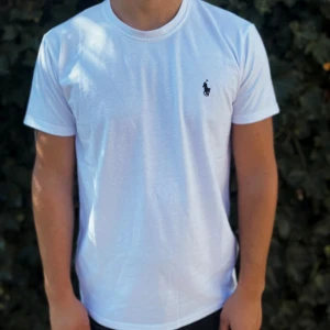 Vit t-shirt från Polo Ralph Lauren - Fräsch vit t-shirt från Polo Ralph Lauren med klassisk rund hals och korta ärmar. Diskret svart logga broderad på bröstet ger en clean och stilren vibe. Tillverkad i mjuk bomull som känns skön mot huden. Perfekt för dig som gillar enkel och snygg design.                                                                                                                               Nypris: 1129kr GORILLAPRIZE:620kr            Skick:10/10 oöppnad         KVITTO MEDKOMMER     