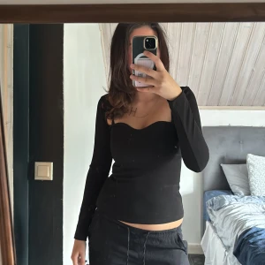 Svart långärmad sweetheart-topp - Säljer en svart långärmad topp med snygg sweetheart-urringning. Modellen är figurnära och har en stilren, enkel look som passar till många outfits. Den är väldigt tajt så skulle säga att den passar dom som har storleken xs💕pris kan diskuteras